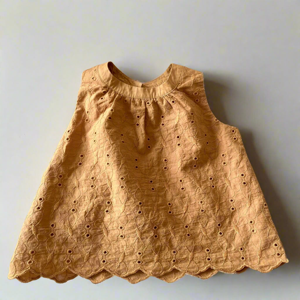 Brown sleeveless top with eyelet details on a textured surface.
