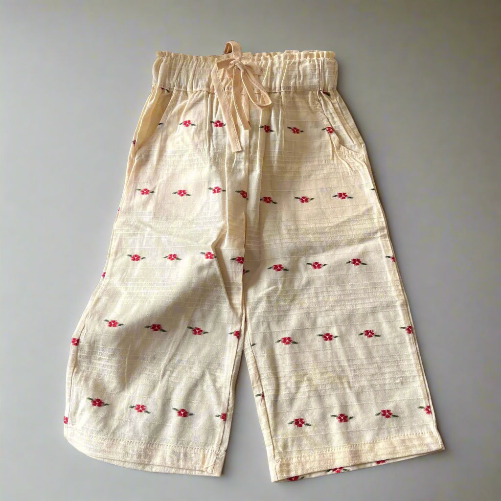 White pants with red floral patterns on a textured surface with a woven basket and donut in the background.