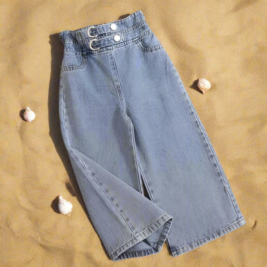 A pair of girls' wide-leg blue jeans laid flat on a wooden surface, showcasing the jeans' design details such as the waistband, pockets, and leg openings.