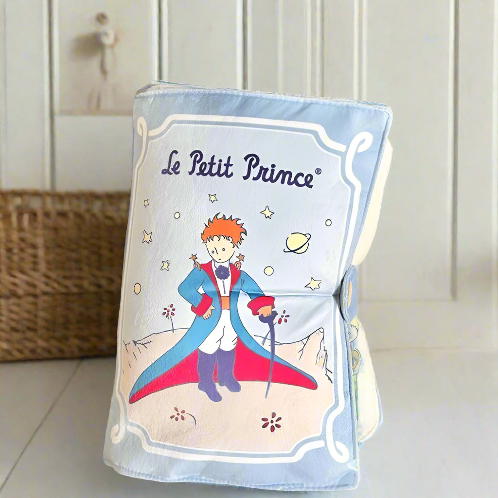 Foldable blanket with 'Le Petit Prince' design on a wooden surface