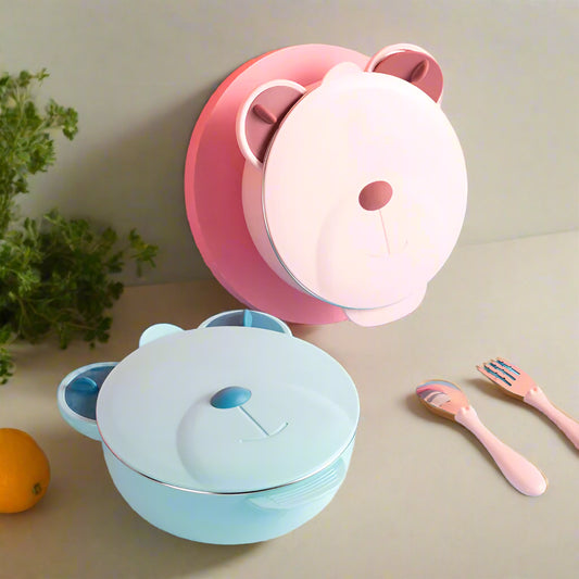 Two bear-shaped lunch boxes, one pink and one blue, on a colorful background with utensils.