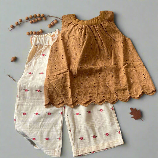 Two pairs of shorts, one mustard yellow with eyelet details and one white with floral patterns, on a textured surface.