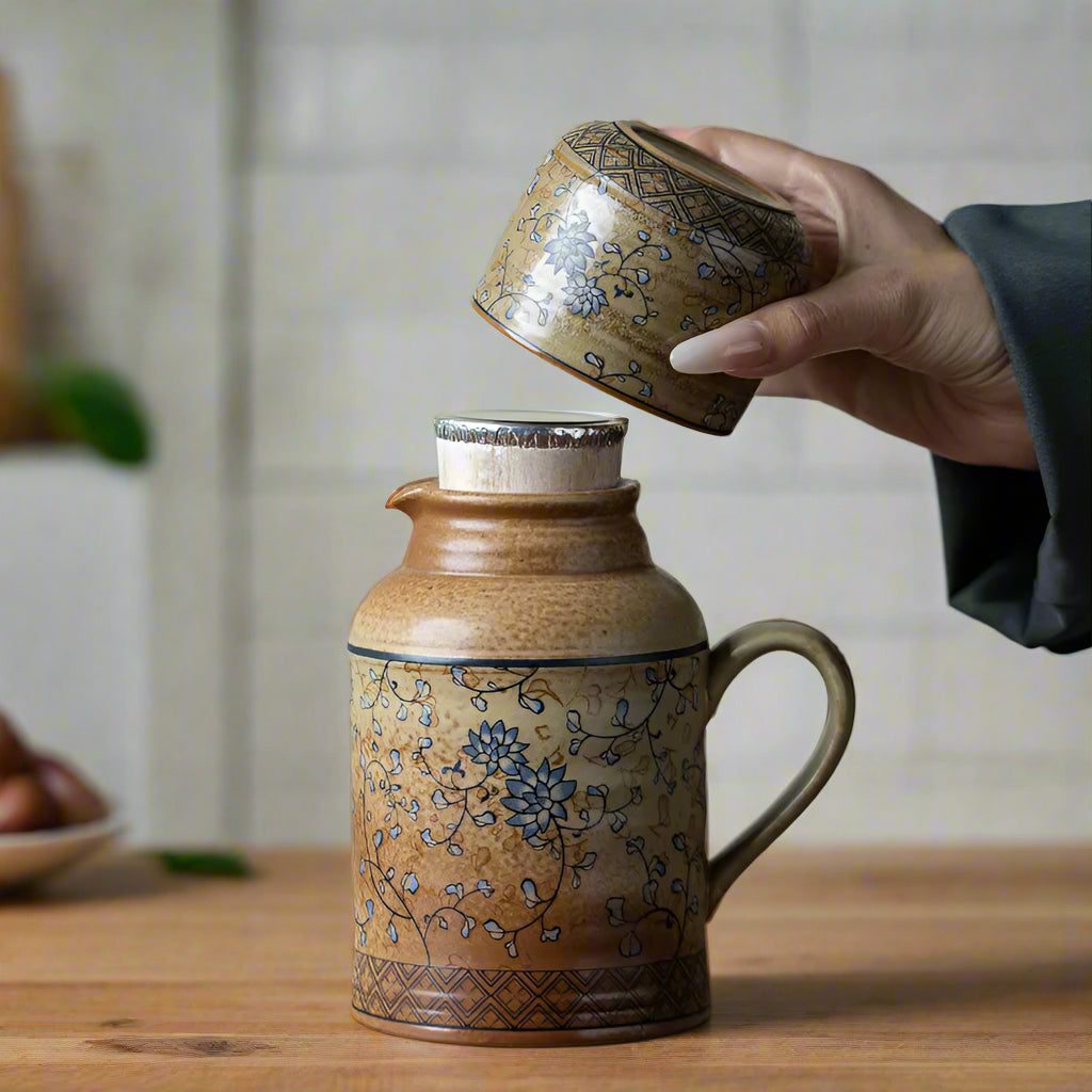 Ceramic jar with floral patterns being held by a hand on a wooden surface.